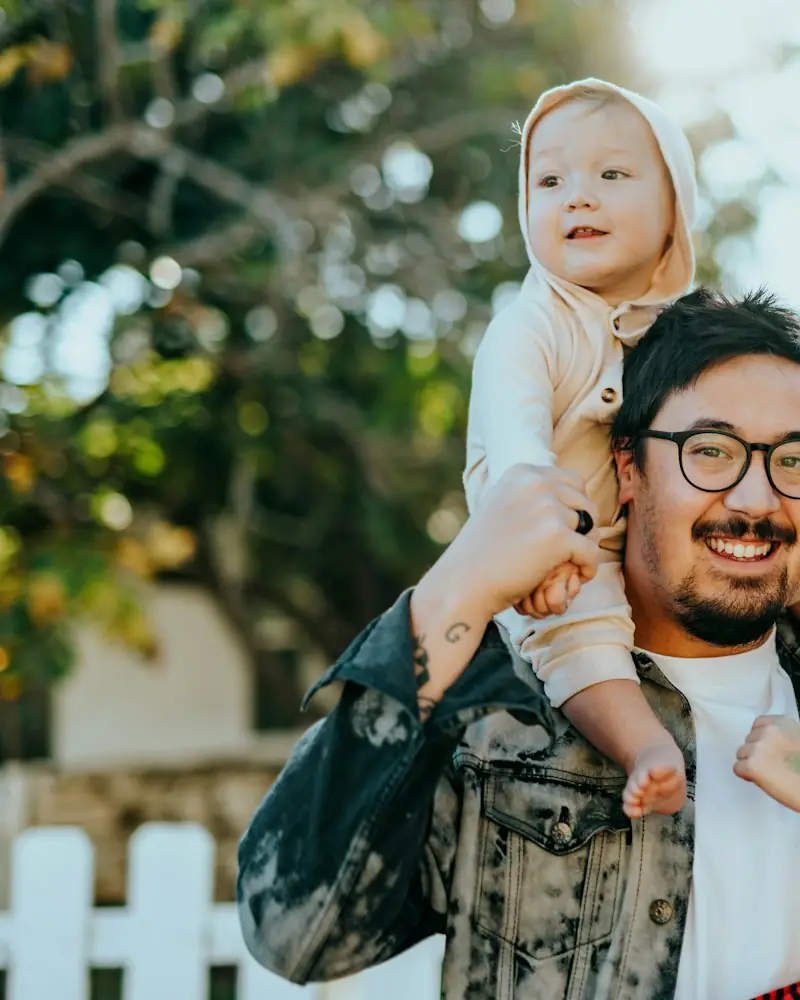 Pai sorrindo com a filha pequena nos ombros